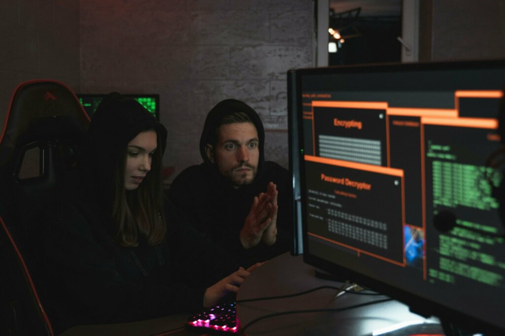 Deux individus en capuche devant un écran affichant un message de chiffrement de données, illustrant une cyberattaque par ransomware.