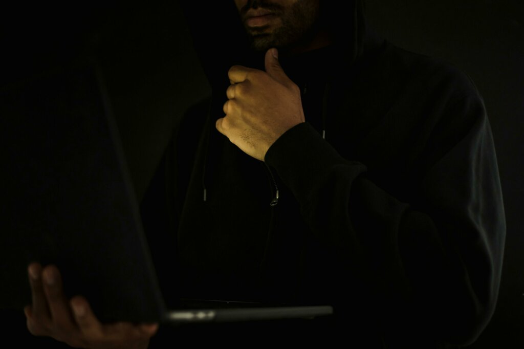 Un individu en capuche tenant un ordinateur portable, représentant une menace cybercriminelle et les risques de ransomware.